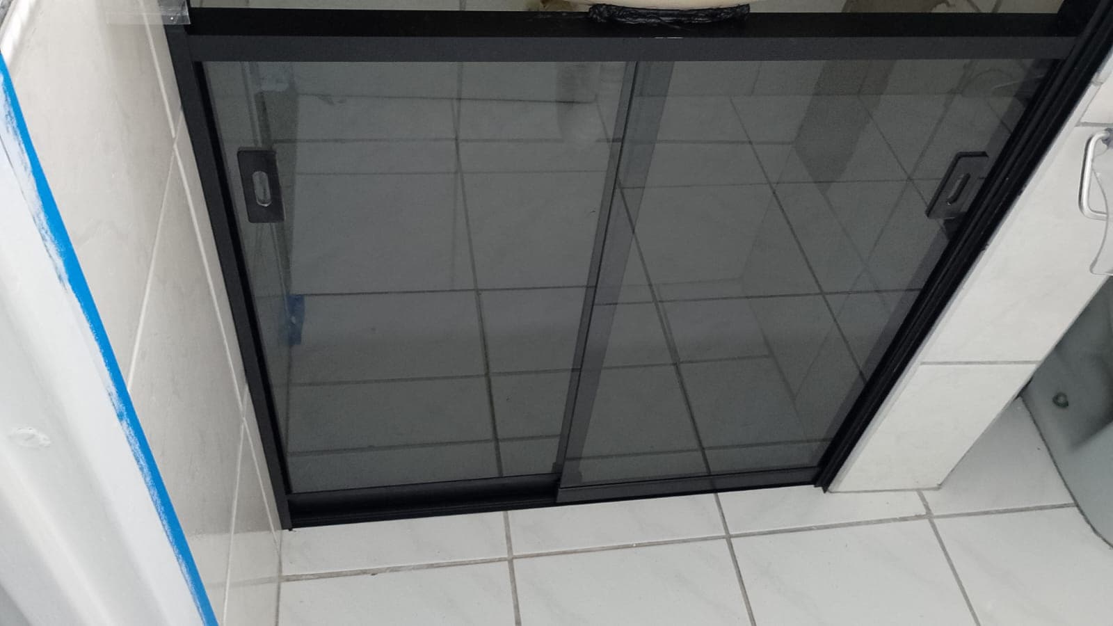 Detalhe de porta de box de vidro com trilho preto sobre piso claro