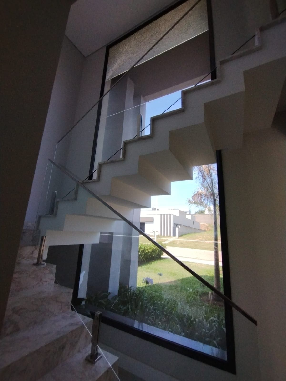 Guarda-corpo de vidro em escada interna com janela ao fundo